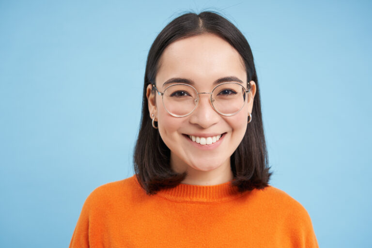 Portrait of smiling beautiful woman in glasses, testing her eyesight, wearing new spectacles, standing over blue background